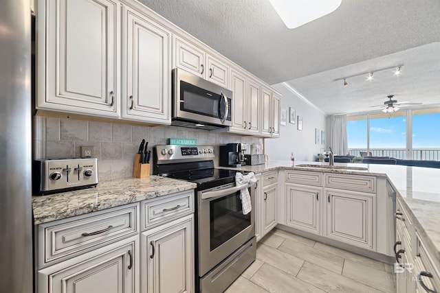 kitchen with ceiling fan, appliances with stainless steel finishes, backsplash, a textured ceiling, and sink