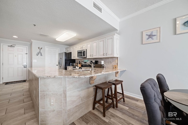 kitchen with white cabinetry, kitchen peninsula, appliances with stainless steel finishes, light stone countertops, and a textured ceiling