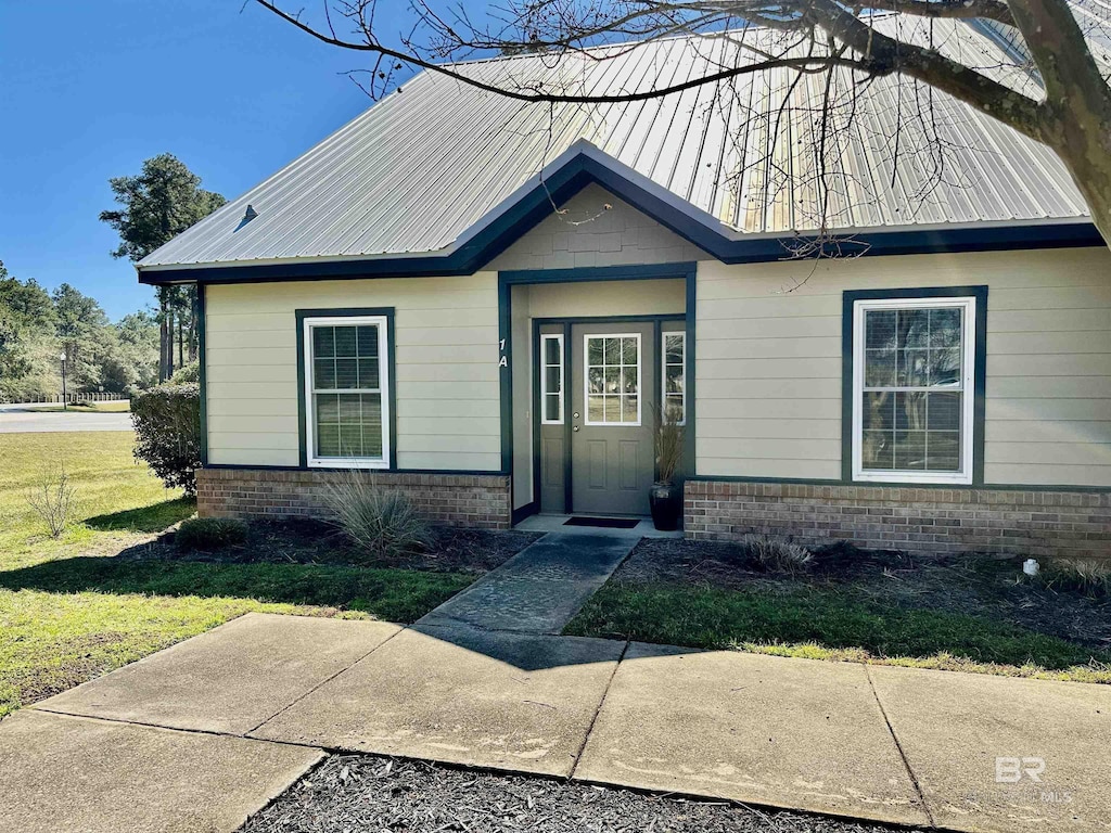 view of front of home featuring brick siding, metal roof, and a front lawn