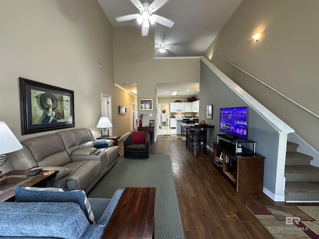 living area featuring a high ceiling, a ceiling fan, baseboards, stairs, and dark wood finished floors