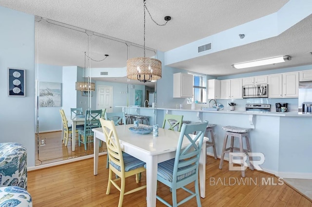 527 Beach Club Trl Unit D710, Gulf Shores, AL 36542 - dining area featuring light wood-type flooring, a textured ceiling, a chandelier, and baseboards