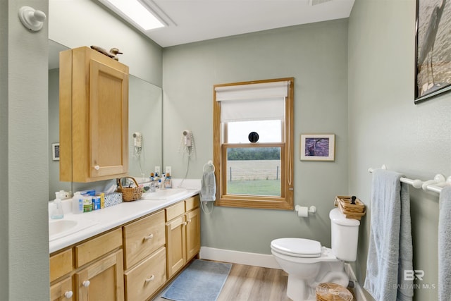 full bathroom featuring wood finished floors, toilet, double vanity, and baseboards