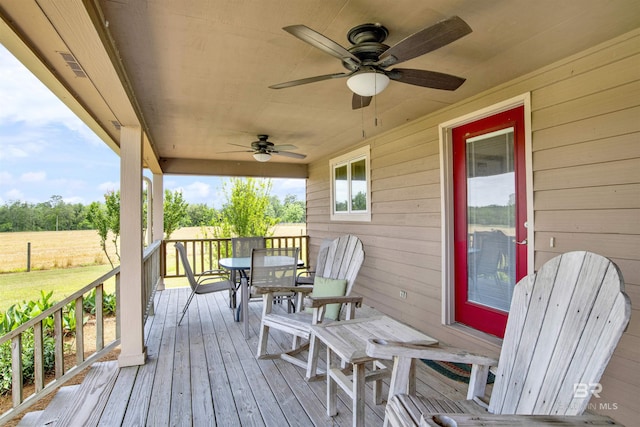wooden deck with outdoor dining space, a ceiling fan, and a lawn