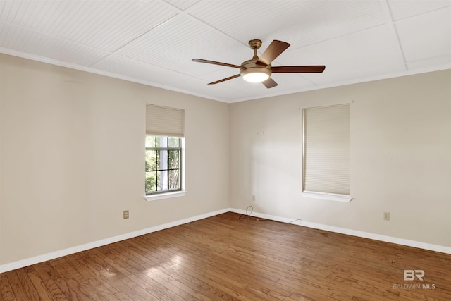 empty room with wood-type flooring, a ceiling fan, baseboards, and crown molding
