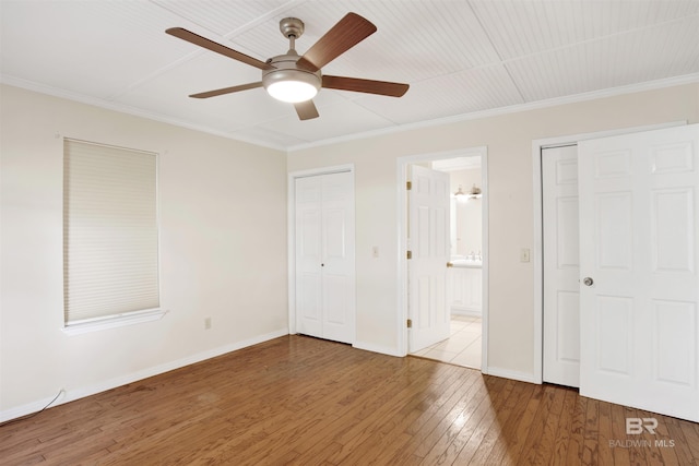 unfurnished bedroom featuring hardwood / wood-style flooring, ornamental molding, baseboards, connected bathroom, and ceiling fan