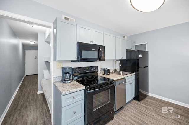 kitchen featuring black appliances, sink, light stone counters, and hardwood / wood-style floors