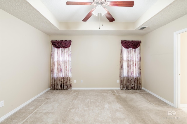 carpeted empty room featuring a raised ceiling, ceiling fan, and plenty of natural light