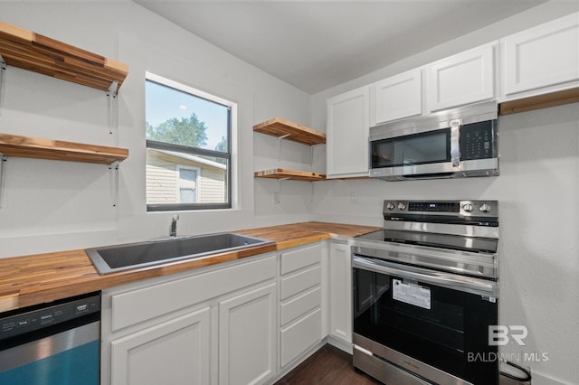 kitchen featuring appliances with stainless steel finishes, butcher block countertops, white cabinetry, and sink