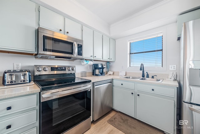 kitchen featuring light wood-style flooring, ornamental molding, a sink, appliances with stainless steel finishes, and light countertops