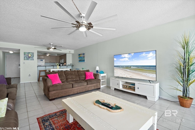 living room with light tile patterned flooring, a ceiling fan, baseboards, and a textured ceiling