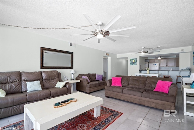 living area featuring light tile patterned floors, a ceiling fan, visible vents, and a textured ceiling
