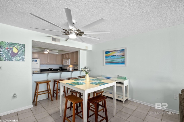 dining area featuring visible vents, a textured ceiling, light tile patterned flooring, baseboards, and ceiling fan