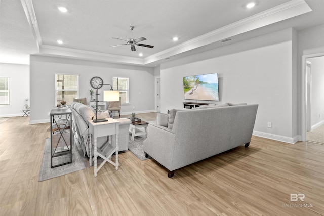 living room featuring ceiling fan, ornamental molding, a raised ceiling, and light wood-type flooring