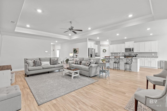 living room featuring ceiling fan, ornamental molding, a tray ceiling, and light hardwood / wood-style floors