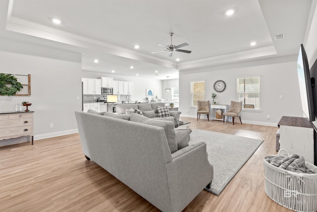 living room with crown molding, a tray ceiling, light hardwood / wood-style floors, and ceiling fan