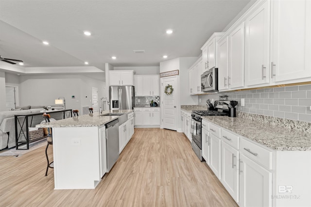 kitchen with a breakfast bar area, light stone counters, a center island with sink, stainless steel appliances, and white cabinets