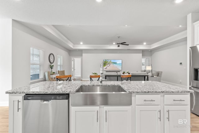 kitchen with appliances with stainless steel finishes, a raised ceiling, an island with sink, and white cabinets