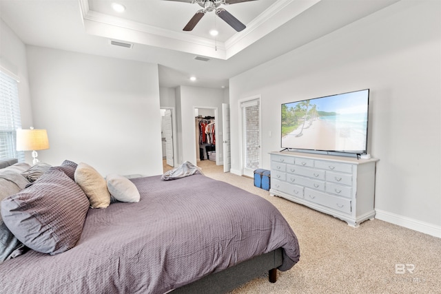 bedroom featuring a spacious closet, light colored carpet, ornamental molding, a tray ceiling, and ceiling fan