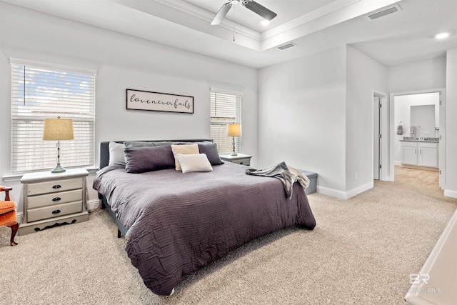 carpeted bedroom with a raised ceiling, crown molding, ceiling fan, and ensuite bath