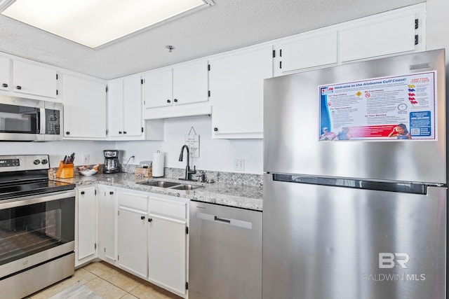 kitchen with appliances with stainless steel finishes, light tile patterned flooring, white cabinetry, light stone countertops, and sink