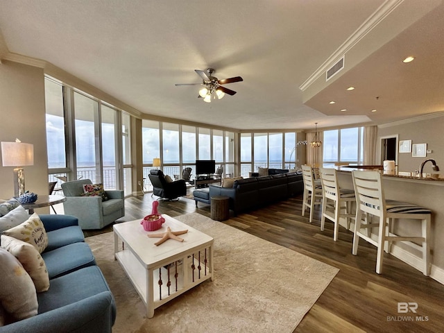 living room with a healthy amount of sunlight, dark hardwood / wood-style flooring, ornamental molding, and ceiling fan with notable chandelier