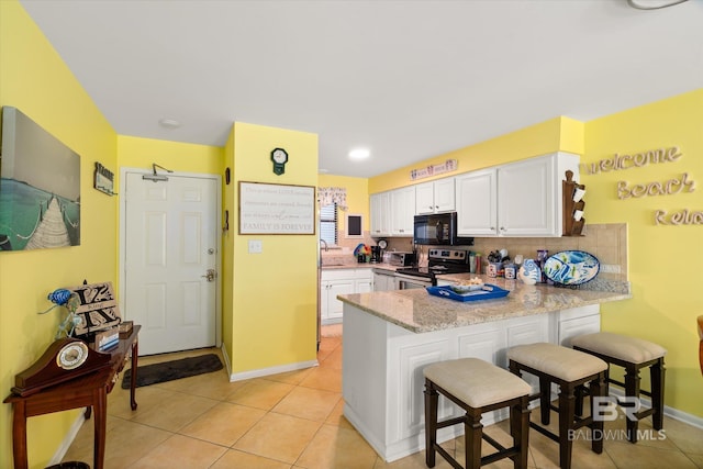 kitchen with black microwave, a peninsula, a breakfast bar, white cabinetry, and stainless steel electric range