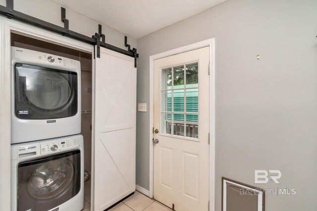 laundry room with light tile patterned flooring, a barn door, and stacked washing maching and dryer