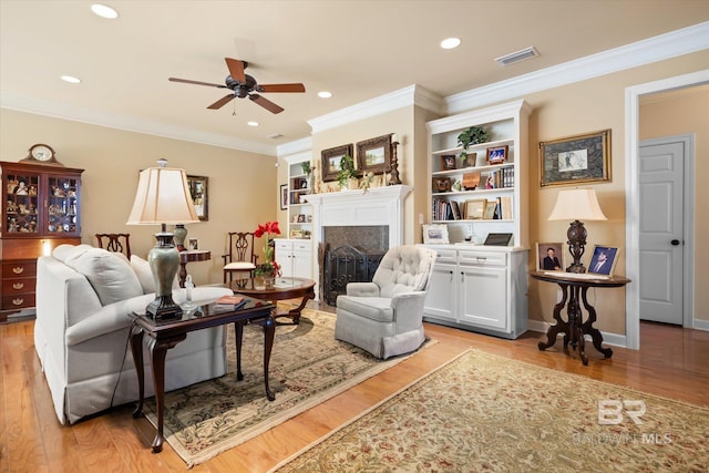 living room featuring ceiling fan, built in shelves, light wood-type flooring, and crown molding