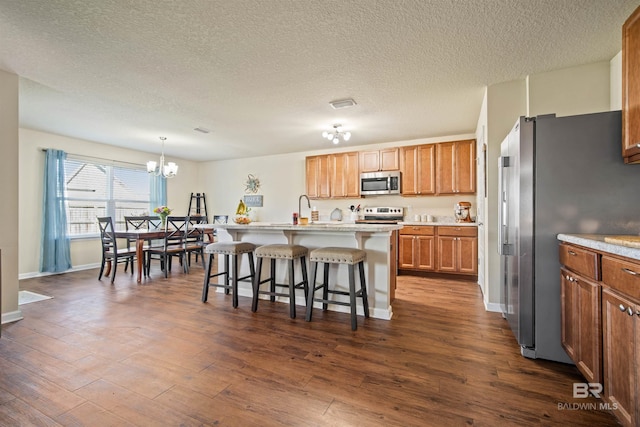 kitchen featuring a breakfast bar, decorative light fixtures, stainless steel appliances, dark hardwood / wood-style flooring, and an island with sink