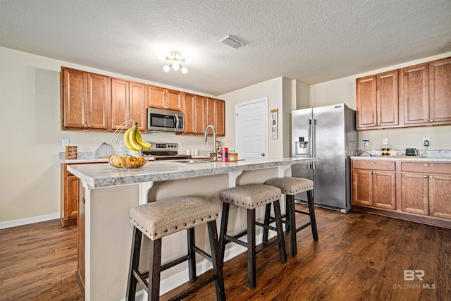 kitchen featuring a kitchen bar, stainless steel appliances, dark hardwood / wood-style flooring, and a kitchen island with sink