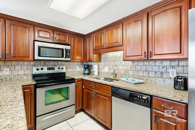 kitchen with backsplash, stainless steel appliances, a textured ceiling, light stone counters, and light tile floors