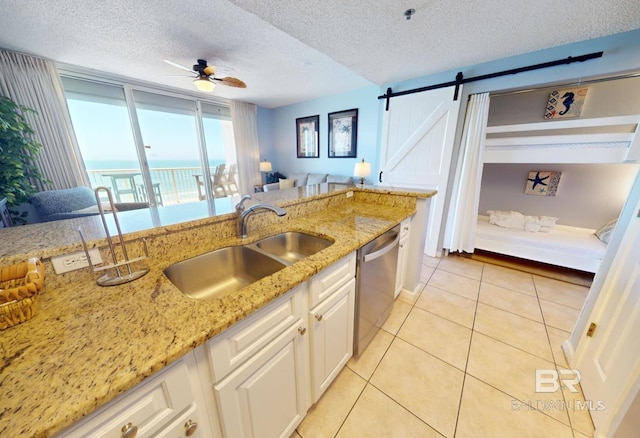 kitchen with a sink, light stone counters, white cabinetry, light tile patterned floors, and dishwasher