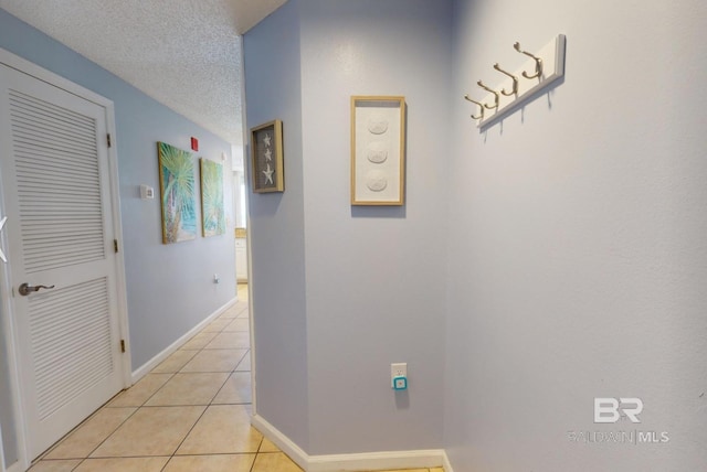 hall featuring light tile patterned floors, baseboards, and a textured ceiling