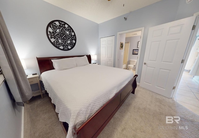 bedroom with light tile patterned floors, a closet, a textured ceiling, light carpet, and connected bathroom