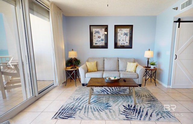 living room featuring a barn door, a textured ceiling, visible vents, and light tile patterned flooring