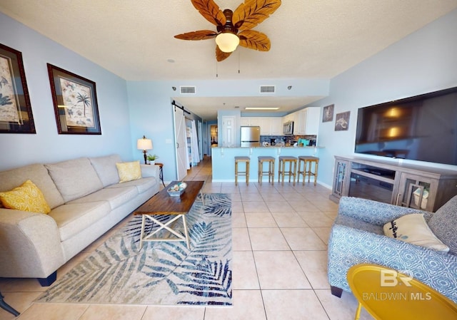 living area featuring a barn door, light tile patterned floors, a ceiling fan, and visible vents