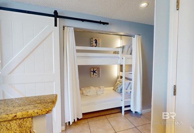 bedroom featuring a barn door, light tile patterned flooring, and a textured ceiling