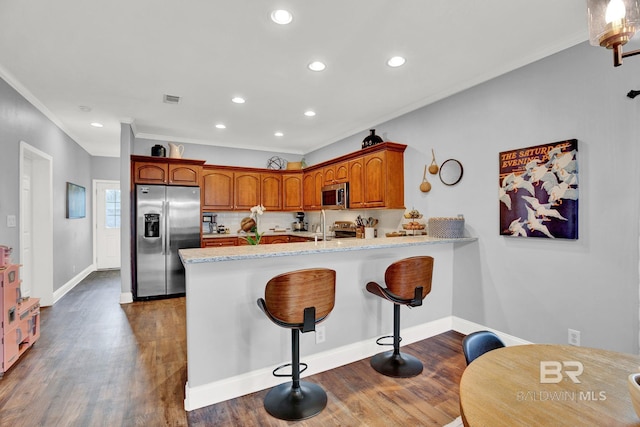 kitchen featuring dark hardwood / wood-style floors, kitchen peninsula, a kitchen bar, stainless steel appliances, and crown molding