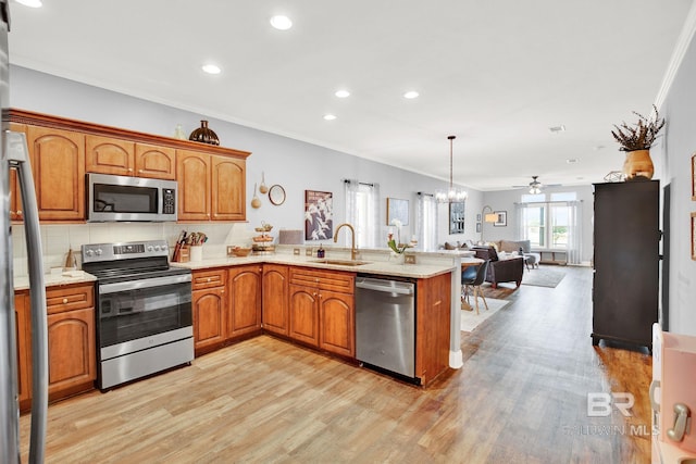 kitchen with pendant lighting, sink, appliances with stainless steel finishes, light wood-type flooring, and crown molding