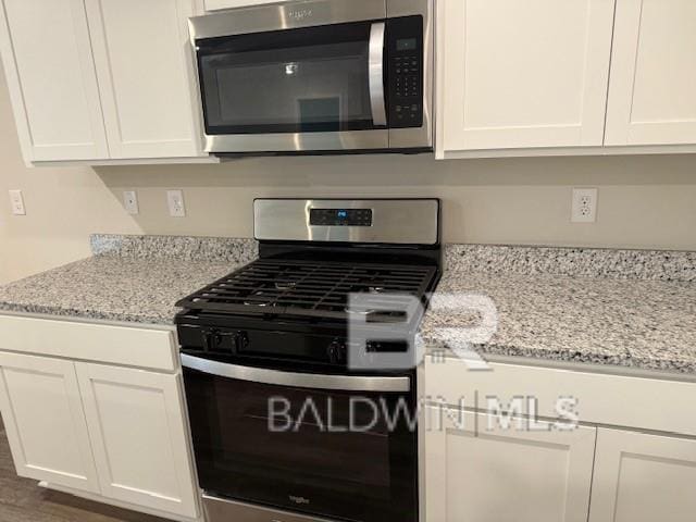 kitchen with stainless steel appliances, white cabinetry, and light stone counters