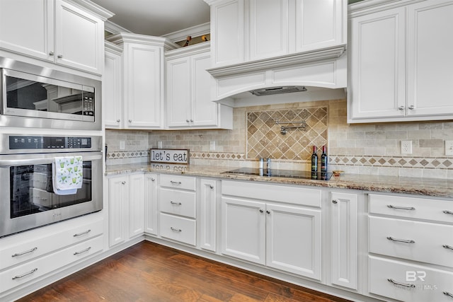 kitchen with dark wood finished floors, appliances with stainless steel finishes, light stone countertops, custom exhaust hood, and white cabinetry