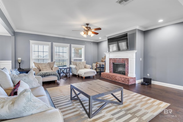 living area featuring visible vents, baseboards, ornamental molding, a brick fireplace, and dark wood finished floors