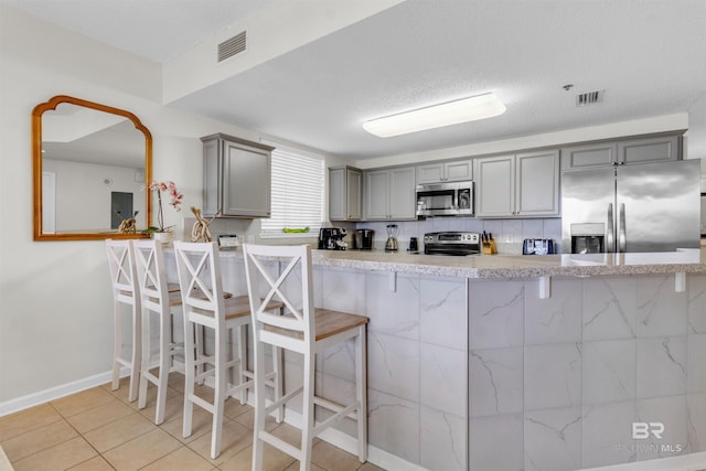 527 Beach Club Trl Unit C110, Gulf Shores, AL 36542 - kitchen with gray cabinetry, appliances with stainless steel finishes, a breakfast bar, light tile patterned floors, and a peninsula