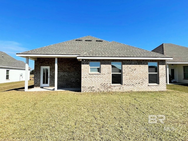 rear view of property featuring a yard, brick siding, roof with shingles, and a patio area