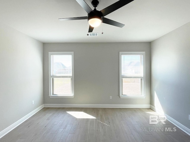 unfurnished room featuring a wealth of natural light, visible vents, baseboards, and wood finished floors