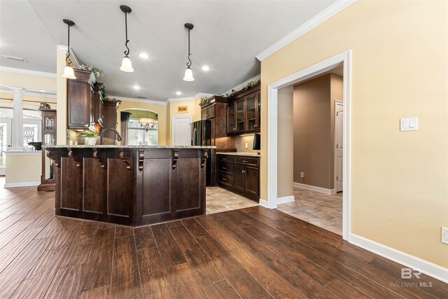 kitchen featuring dark brown cabinets, backsplash, hanging light fixtures, ornate columns, and hardwood / wood-style floors