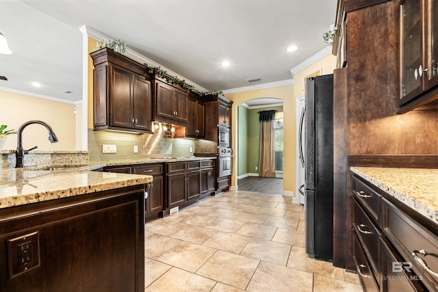 kitchen featuring dark brown cabinetry, oven, sink, tasteful backsplash, and black refrigerator