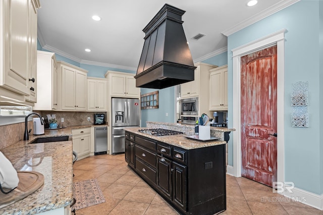 kitchen featuring a sink, dark cabinets, premium range hood, cream cabinetry, and appliances with stainless steel finishes