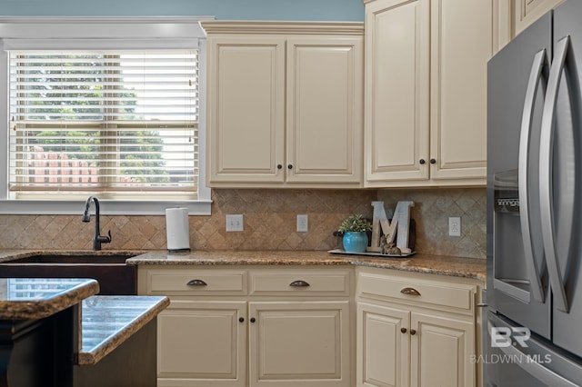 kitchen featuring light stone counters, tasteful backsplash, a sink, stainless steel fridge with ice dispenser, and cream cabinetry