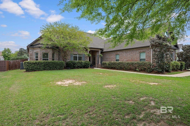view of front facade featuring brick siding, fence, and a front yard